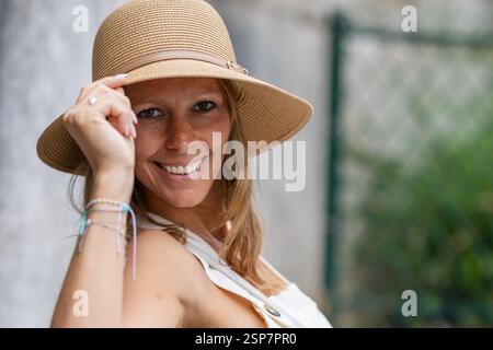 Femme souriante en chapeau de paille posant avec confiance à l'extérieur Banque D'Images