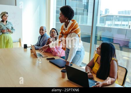 Une femme noire confiante se tient debout et mène une discussion dans une salle de conseil remplie de membres du conseil d'administration exclusivement féminins. L'environnement professionnel reflète l'équipe Banque D'Images
