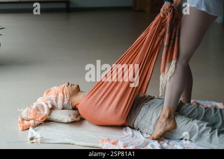 Un professionnel guide une personne à travers une séance d'étirement relaxante en utilisant des accessoires en tissu doux dans un studio tranquille, favorisant le bien-être et l'harmonie Banque D'Images