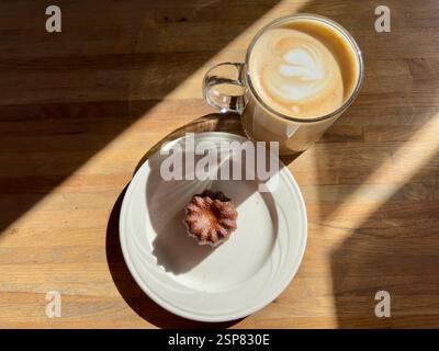 Latte avec art latte coeur et un canelé sur une assiette au soleil Banque D'Images