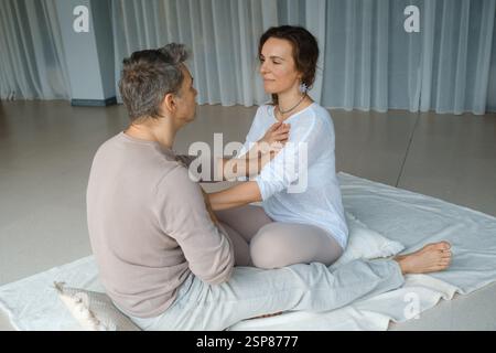 Deux personnes pratiquent la pleine conscience dans un studio apaisant, en se concentrant sur la connexion émotionnelle et la relaxation. Ils s'assoient étroitement sur un tapis mou, favorisant t Banque D'Images