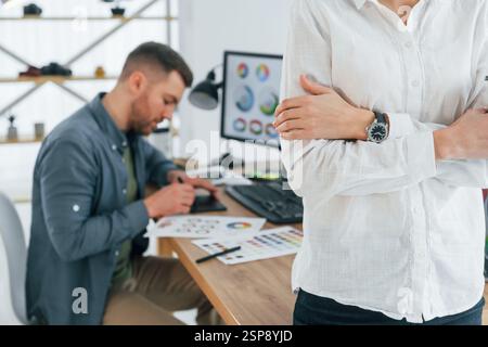 Femme debout devant l'homme qui est assis près de la table. Deux designers travaillant ensemble au bureau. Banque D'Images