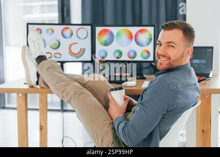Assis sur la chaise, détendu. Concepteur masculin travaillant dans le bureau en utilisant un PC. Banque D'Images
