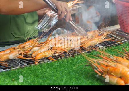 gros plan de crevettes de rivière fraîches grillées au-dessus d'une flamme chaude dans un étal de nourriture de rue animé. Leurs coquillages orange vif et leur arôme fumé capturent Banque D'Images