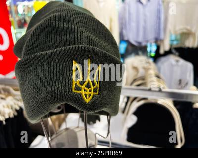 Lviv, Ukraine - 13 février 2025 : bonnet vert avec emblème jaune ukrainien, affiché contre des cintres avec divers vêtements. Banque D'Images