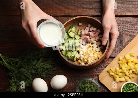 Femme faisant de la soupe okroshka avec du kéfir à la table en bois, vue de dessus Banque D'Images