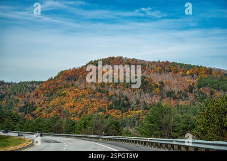 Une autoroute sinueuse traverse le feuillage d'automne vibrant dans le Vermont, mettant en vedette des arbres d'automne colorés dans un ciel bleu vif. Banque D'Images