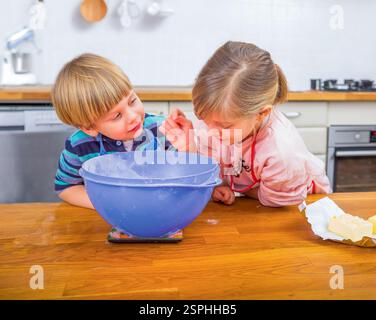 Deux enfants aiment cuisiner dans une cuisine moderne et lumineuse, mesurer les ingrédients et partager des moments de joie. Banque D'Images