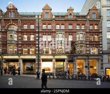 Piétons et vélos devant les magasins Cotswold et Davidson sur Strand London. Les gens font du shopping et profitent de la soirée. Banque D'Images