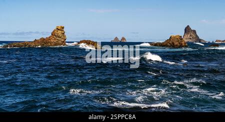 Une vue panoramique des formations rocheuses émergeant de l'océan, avec des vagues s'écrasant contre eux sous un ciel bleu clair. Le paysage comporte plusieurs ro Banque D'Images
