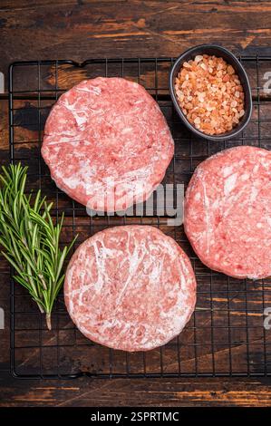 Pâtés de viande congelés prêts à griller, viande forcée de porc et de bœuf pour les hamburgers. fond en bois. vue de dessus Banque D'Images
