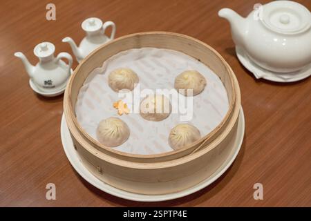 Dim sum traditionnel composé de petits pains cuits à la vapeur servis dans un cuiseur vapeur en bambou, accompagnés de thé et de condiments dans des pichets à cercueil. Banque D'Images