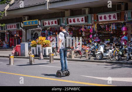 Shanghai, Chine - 27 septembre 2018 : un jeune homme chinois monte une planche à roulettes sur la rue après une rangée de vélos et de scooters. Banque D'Images