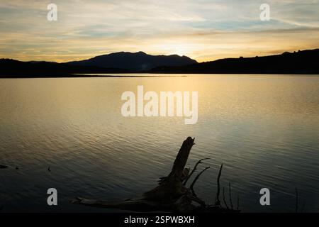 Beau coucher de soleil au réservoir de Beniarres avec des reflets dorés et le parc naturel de la Sierra de Mariola en arrière-plan, Espagne Banque D'Images