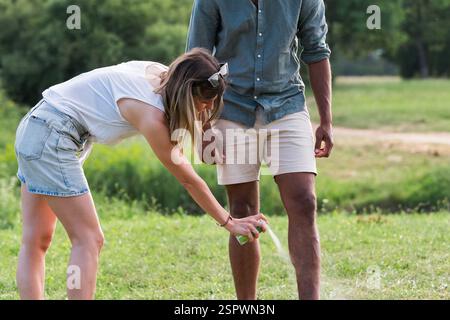 Jeune couple pulvérisant un répulsif contre les tiques sur ses jambes et ses bras pendant un voyage nature d'été Banque D'Images