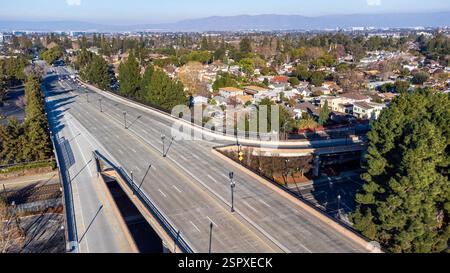 Vue aérienne d'un passage supérieur vide dans un quartier de banlieue, entouré d'arbres et de maisons résidentielles, avec des montagnes lointaines sous un ciel bleu clair Banque D'Images
