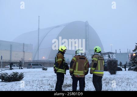 Ukraine. 14 février 2025. RÉGION DE KIEV, UKRAINE - 14 FÉVRIER 2025 - des secouristes regardent le nouveau confinement sûr de la centrale nucléaire de Tchernobyl qui a été touché par un drone d'attaque russe avec une ogive explosive dans la nuit du vendredi 14 janvier, dans la région de Kiev, au nord de l'Ukraine. La structure mise en place en 2016 protège les restes du réacteur 4 détruit lors de la catastrophe de Chornobyl en 1986. (Photo de Volodymyr Tarasov/Ukrinform) crédit : Ukrinform/Alamy Live News Banque D'Images