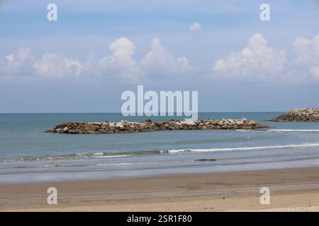 île de formation rocheuse artificielle avec de douces vagues se brisant sur des rivages sablonneux sous un ciel partiellement nuageux Banque D'Images