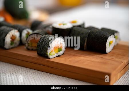 Un gros plan de rouleaux de sushi fraîchement préparés avec du saumon, du concombre et du poivron, enveloppés dans du nori et placés sur une planche de bois. Banque D'Images