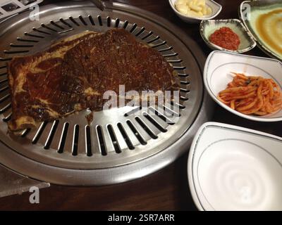 Barbecue coréen. Le ventre de porc mariné grésille sur un gril rond. Des tranches de kimchi et de gousses d'ail complètent la viande. Un repas partagé avec des proches dans le Sud Banque D'Images