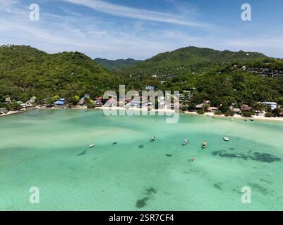 Un village serein en bord de mer niché près de collines verdoyantes avec de l'eau turquoise et des bateaux ancrés. Koh Tao, Thaïlande. Banque D'Images