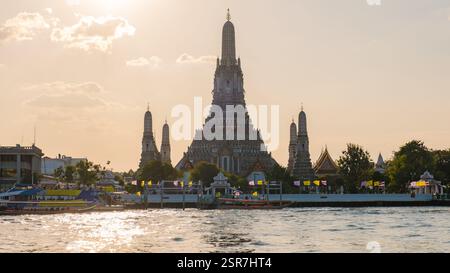 Les rayons dorés illuminent Wat Arun tandis que les bateaux glissent le long de la rivière Chao Phraya. Ce temple emblématique présente des détails complexes dans un ciel vibrant, incarnant l'allure des Bangkoks au crépuscule. Banque D'Images