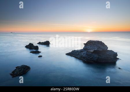 Lever de soleil sur la mer Méditerranée à Cabo de Palos, Carthagène, région de Murcie, Espagne, avec des roches volcaniques émergeant des eaux bleues calmes Banque D'Images