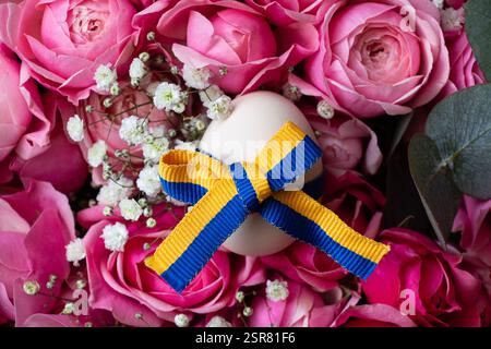 Ruban de drapeau ukrainien sur l'oeuf de poule, l'oeuf repose sur le bouquet de roses roses roses, vacances de Pâques en Ukraine Banque D'Images