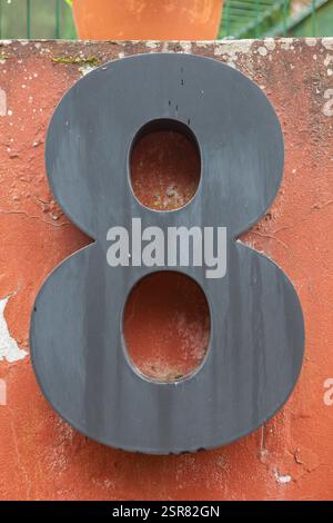 Maison numéro 8. Fer peint noir sur mur rouge altéré. Maisons avec concept de personnalité Banque D'Images