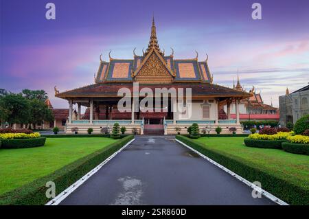 Vue de face du Palais Royal à Phnom Penh, Cambodge, au coucher du soleil, mettant en valeur l'architecture khmère, les toits dorés, un jardin paysager, et un grand père Banque D'Images