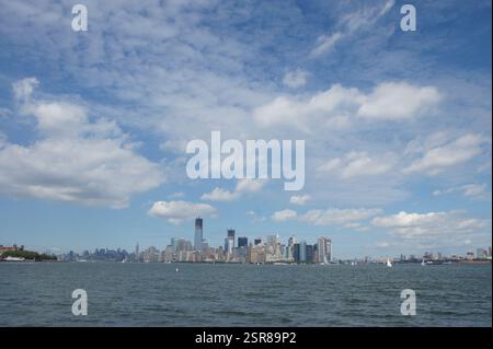 New York, les gratte-ciel emblématiques de Manhattan traversent un ciel bleu clair de nuages tortueux. La Statue de la liberté se dresse fièrement au premier plan, un hors du temps Banque D'Images