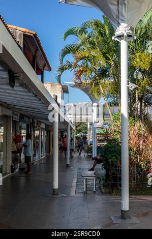 Couloir commercial ombragé du centre commercial Rua dos Biquínis dans le quartier Gamboa avec des magasins, un aménagement paysager vert et des gens se promenant sous un après-midi d'été. Banque D'Images