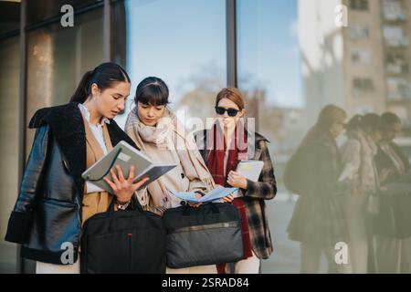 Trois femmes d'affaires collaborant à l'extérieur tout en examinant des documents dans un cadre professionnel Banque D'Images