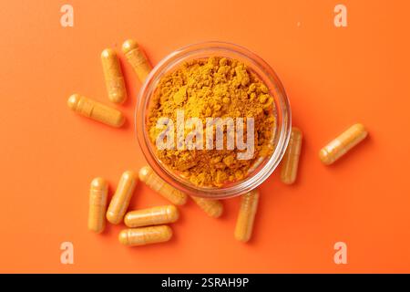 Poudre de curcuma dans un bol et capsules sur fond orange, plat Banque D'Images