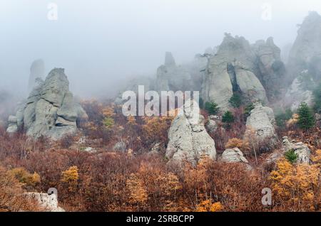 Un brouillard étrange enveloppe les formations rocheuses accidentées de Crimée, créant une atmosphère mystérieuse. Le feuillage d'automne ajoute un contraste éclatant aux pierres grises. Angle bas Banque D'Images