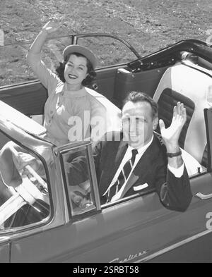 Couple d'âge moyen dans leur voiture cabriolet avec le toit en bas souriant et agitant à la caméra Banque D'Images