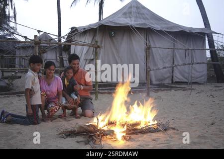 Parent indien sud-asiatique et enfants assis devant un feu de camp appréciant la chaleur dans le froid sur le bord de mer, Shiroda, Dist. Sindhudurga, Maharashtra, Indi Banque D'Images