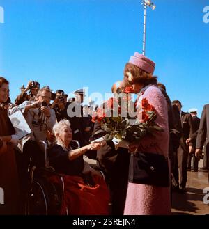 La première dame Jacqueline Kennedy (tenant un bouquet de roses rouges) serre la main à Annie Dunbar (en fauteuil roulant) après son arrivée à Love Field à Dallas, Texas ; le président John F. Kennedy (principalement caché, derrière MRS Kennedy) salue un homme non identifié. Tous les autres ne sont pas identifiés. Date : 22 novembre 1963 Banque D'Images