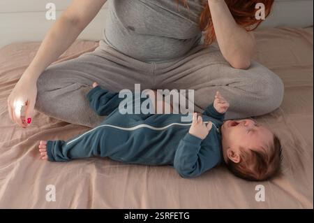 Une femme caucasienne est assise sur un lit à côté d'un bébé qui pleure. Dépression du post-partum. Banque D'Images