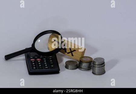 L'image montre une calculatrice noire, une loupe, un bloc de bois avec le mot 'TAX' écrit dessus, et plusieurs piles de pièces de monnaie. Banque D'Images