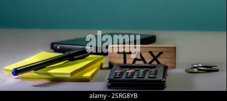 L'image montre une calculatrice noire, un bloc de bois avec le mot 'TAX' écrit dessus, et deux piles de pièces de monnaie. La calculatrice dispose d'un écran d'affichage et Banque D'Images