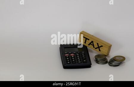 L'image montre une calculatrice noire, un bloc de bois avec le mot 'TAX' écrit dessus, et deux piles de pièces de monnaie. La calculatrice dispose d'un écran d'affichage et Banque D'Images