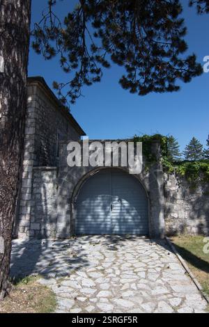 Mur de pierre rustique avec une porte en arc bleu entourée d'ombre naturelle et de briques dispersées, évoquant la sérénité et l'intemporalité dans un cadre rural ou historique Banque D'Images