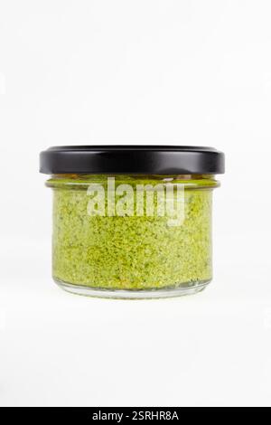 Pot en verre scellé rempli de sauce pesto verte à base de basilic, d'ail, de fromage et de pignons de pin, placé sur un fond blanc Banque D'Images