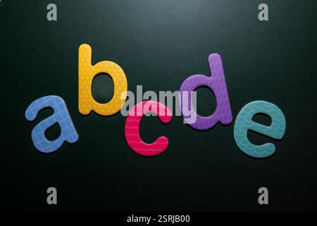 Lettres en mousse colorées a, b, c, d, e disposées sur un fond sombre, symbolisant l'apprentissage précoce, l'alphabétisation et le design créatif. Banque D'Images