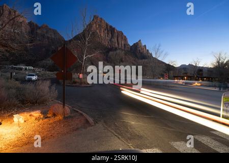 Parc national de Zion, Utah. Voitures se déplaçant le long de la route au crépuscule, avec les montagnes emblématiques de Zion Canyon en arrière-plan. Banque D'Images
