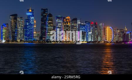 Panorama du centre-ville d'affaires de Doha illuminé la nuit, avec des gratte-ciel modernes et la mer au premier plan, Qatar Banque D'Images