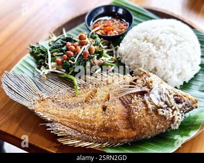 Une portion de poisson gourami frit est servie avec une salade de légumes jukut urab, du riz et du sambal bawang, présentés sur une feuille de banane Banque D'Images
