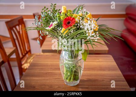 Bouquet de fleurs mélangées colorées dans un vase transparent placé sur une table en bois Banque D'Images