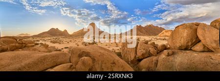 Sugarloaf, Spizkoppe, et Little Spizkoppe au coucher du soleil, un avion avec des buissons et de gros rochers au premier plan, Namibie, Afrique. Banque D'Images